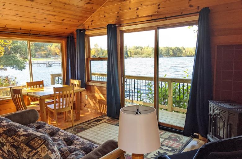 Lakeside facing living room with patio doors, futon, chair, gas fireplace, and kitchen table.